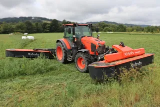 Oranžový traktor Kubota se žacím strojem na louce.