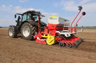 Traktor s červeno-bílým secím strojem Pöttinger na poli.