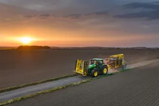 Traktor se secím strojem Bednar na polní cestě při západu slunce.