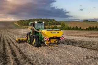 Traktor s žlutým zásobníkem Bednar při práci na poli za soumraku.