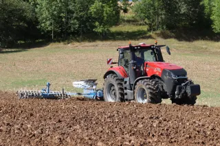 Červený traktor Case IH Magnum s pluhem při orbě pole.
