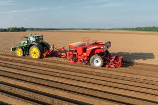 Traktor táhne červený sazeč brambor Grimme po poli.