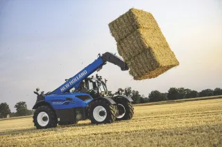 Modrý teleskopický manipulátor New Holland zvedá balík slámy.