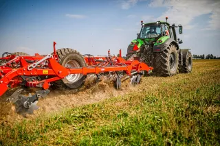 Traktor s červeným kypřičem Kuhn při polní ukázce.