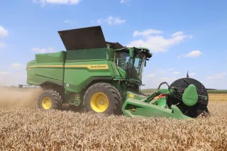 Zelená sklízecí mlátička John Deere sklízí obilí.