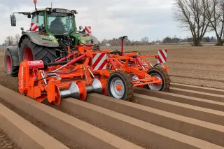 Traktor s oranžovou hrobkovací frézou Struik na poli.