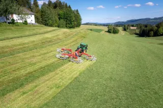 Traktor s čtyřrotorovým shrnovačem Pöttinger na louce
