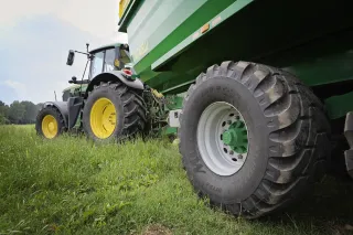 Traktor s velkým zeleným návěsem na louce