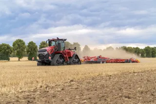 Červený pásový traktor táhne zemědělský stroj po poli