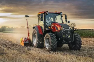 Červený traktor Case IH na poli při západu slunce
