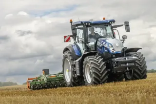 Modrý traktor New Holland na poli pod zamračenou oblohou