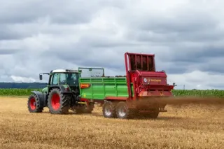 Traktor táhne zelené rozmetadlo Strautmann po poli