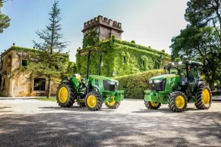 Dva zelené traktory John Deere před historickou budovou