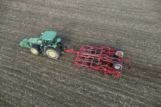 Traktor táhne červený kultivátor po strništi