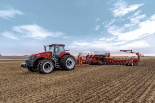 Červený traktor Case IH se secím strojem na poli