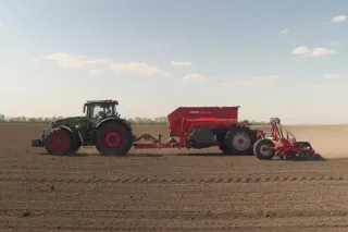 Traktor táhne červený secí stroj HORSCH po poli