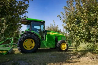 Zelený traktor John Deere v sadu