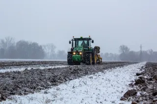Zelený traktor při práci na zasněženém poli