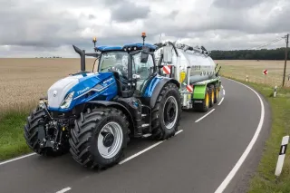 Modrý traktor New Holland táhne cisternu po silnici