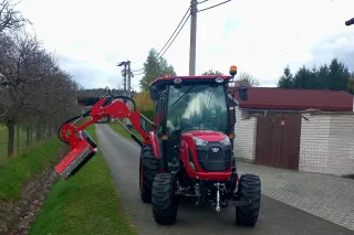 Červený traktor TYM s ramenovou sekačkou u silnice