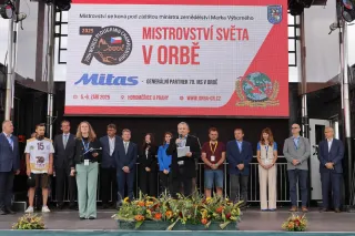 Skupina účastníků na pódiu pod nápisem Mistrovství světa v orbě, uprostřed muž hovoří do mikrofonu.