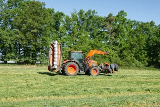 Oranžový traktor se žacím strojem na louce