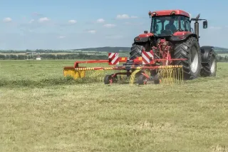 Červený traktor s červeným shrnovačem sena na louce