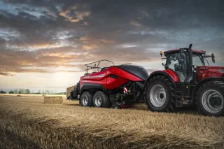 Červený traktor Case IH s lisem na balíky na poli