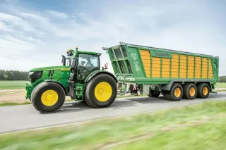 Zelený traktor John Deere s návěsem na louce