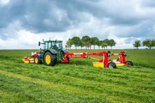 Zelený traktor s žacím strojem Pöttinger na louce