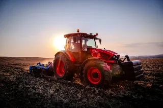 Červený traktor při práci na poli za západu slunce