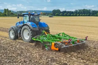 Modrý traktor s připojeným půdozpracujícím strojem na poli