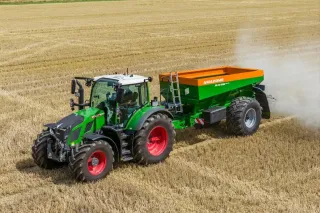 Zelený traktor s rozmetadlem hnojiva na poli