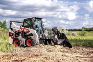 Bílý smykem řízený nakladač Bobcat na louce
