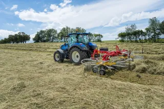 Modrý traktor se shrnovačem sena na louce