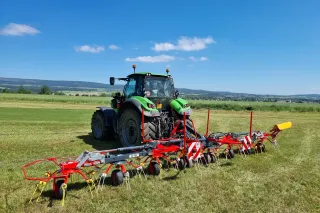 Zelený traktor s obracečem píce ROZMITAL na louce