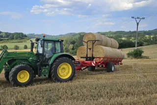 Zelený traktor s nakladačem a lisem na poli