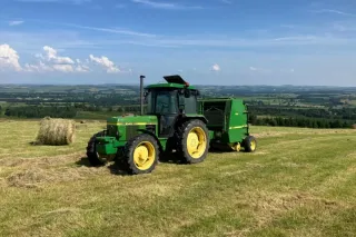 Zelený traktor John Deere s lisem na louce