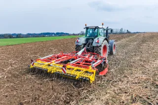Červený kypřič Pöttinger za traktorem na poli