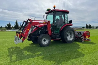 Červený traktor TYM s čelním nakladačem na travnaté ploše