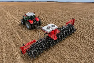 Červený traktor Massey Ferguson se secím strojem na poli