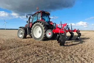 Červený traktor na poli pod zataženou oblohou