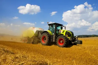 Světle zelený traktor Claas s lisem na poli.