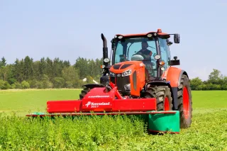 Červený traktor se žacím strojem Kverneland na louce.