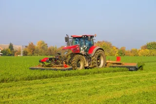 Červený traktor Case IH Optum 300 se žacími stroji SIP na louce.
