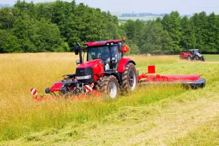 Červený traktor Case IH se žací kombinací na louce.