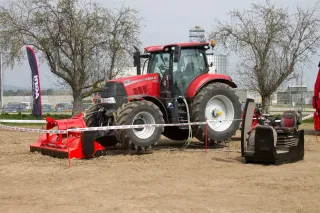 Červený traktor Case IH s předním strojem na výstavní ploše.