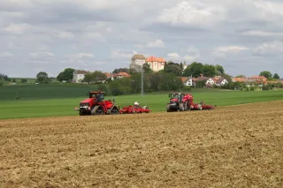 Dva červené traktory Case IH na poli pod hradem.