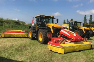 Žluté traktory JCB se žacími stroji na louce.