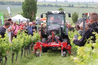 Traktor s vinohradnickým nářadím mezi řádky révy před návštěvníky jarmarku